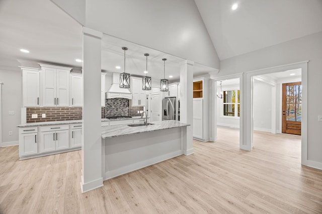 kitchen with light stone countertops, sink, white cabinets, custom range hood, and light wood-type flooring