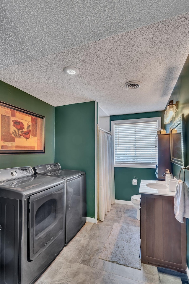 washroom with washer and dryer, a textured ceiling, and sink