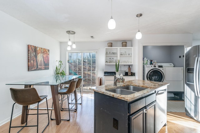 kitchen with light stone countertops, sink, stainless steel appliances, an island with sink, and washer and clothes dryer