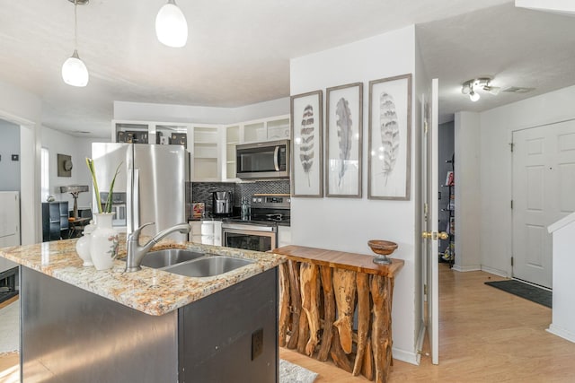 kitchen featuring sink, stainless steel appliances, light hardwood / wood-style floors, decorative light fixtures, and a center island with sink