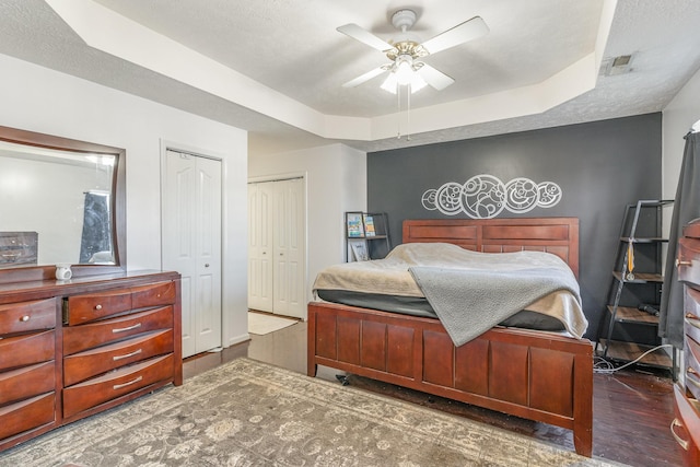 bedroom featuring a textured ceiling, dark hardwood / wood-style floors, a raised ceiling, and ceiling fan