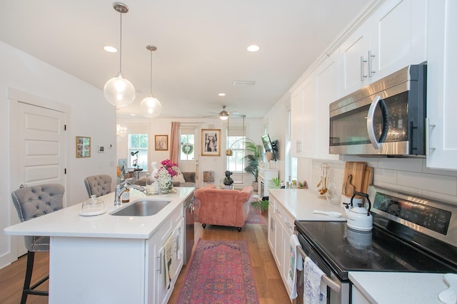 kitchen featuring white cabinetry, sink, stainless steel appliances, a kitchen breakfast bar, and decorative light fixtures