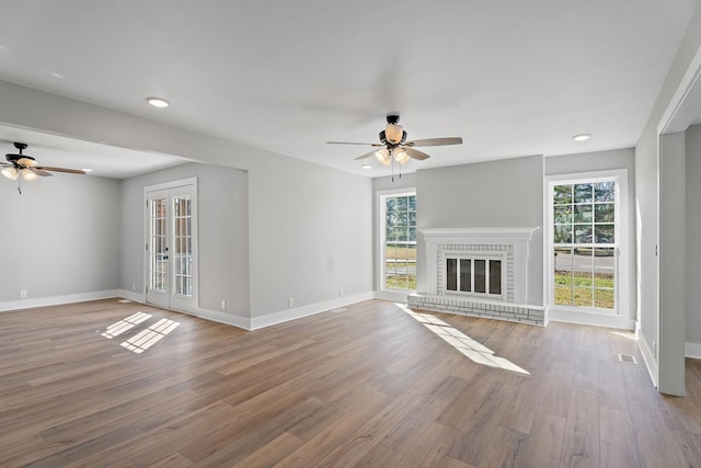 unfurnished living room featuring ceiling fan, a healthy amount of sunlight, light wood-type flooring, and a fireplace