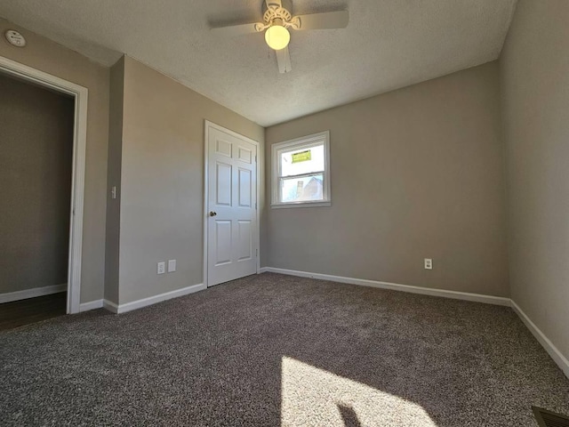 unfurnished bedroom featuring a textured ceiling, dark carpet, and ceiling fan