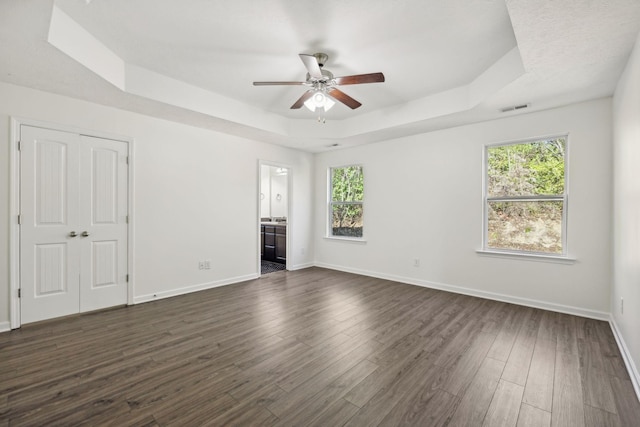 empty room featuring ceiling fan, a raised ceiling, and dark wood-type flooring