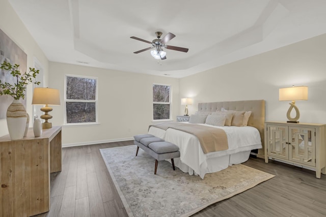 bedroom with a ceiling fan, a raised ceiling, baseboards, and wood finished floors