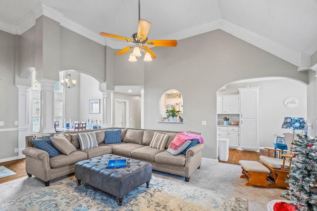 living room with decorative columns, a towering ceiling, light wood-type flooring, ceiling fan with notable chandelier, and crown molding