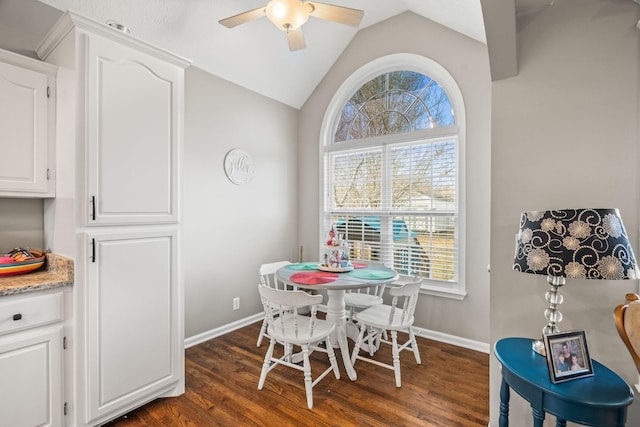 dining space featuring a ceiling fan, baseboards, vaulted ceiling, and dark wood-type flooring