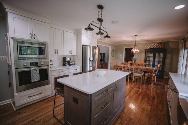 kitchen with white cabinetry, a center island, hanging light fixtures, stainless steel appliances, and dark hardwood / wood-style flooring