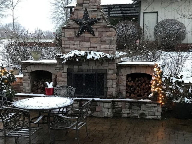 snow covered patio featuring an outdoor stone fireplace