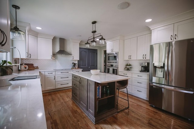 kitchen featuring appliances with stainless steel finishes, wall chimney range hood, decorative light fixtures, white cabinets, and a kitchen island