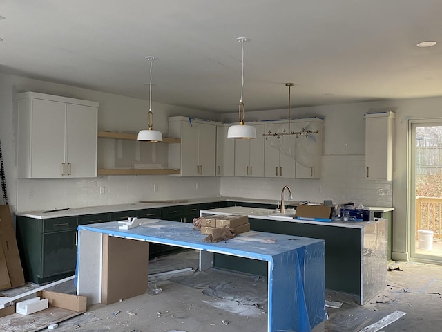 kitchen featuring tasteful backsplash, sink, decorative light fixtures, stovetop, and an island with sink