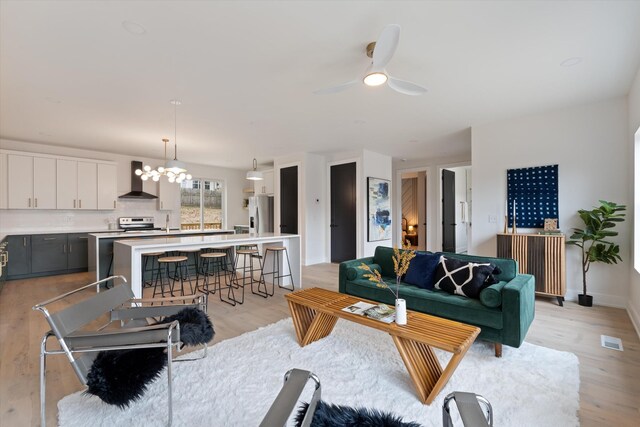 living area with visible vents, light wood-style flooring, baseboards, and ceiling fan with notable chandelier