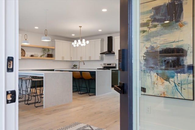 kitchen featuring white cabinets, wall chimney range hood, pendant lighting, and a kitchen breakfast bar