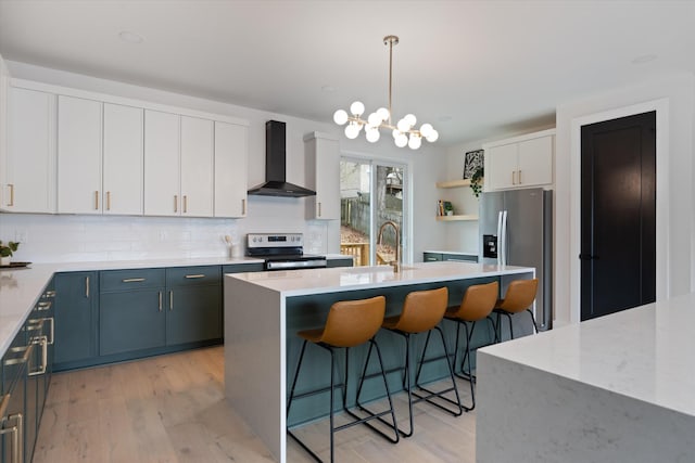 kitchen with white cabinets, an island with sink, stainless steel appliances, wall chimney range hood, and pendant lighting