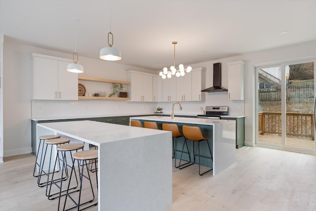 kitchen featuring open shelves, light countertops, wall chimney range hood, an island with sink, and a kitchen breakfast bar