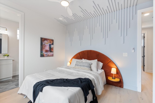 bedroom with light wood-style floors, ensuite bath, and baseboards