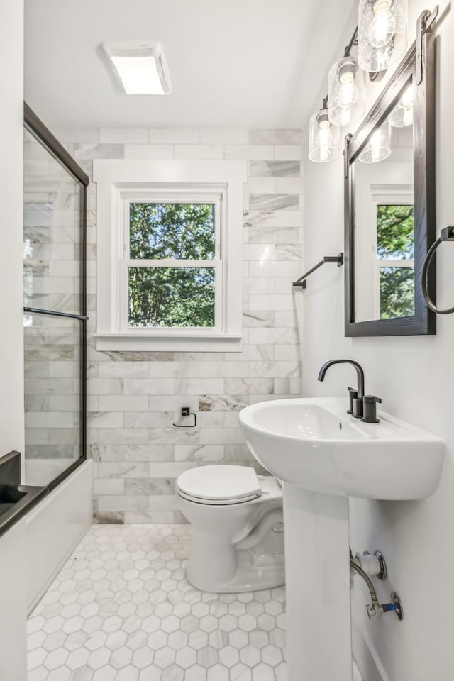 bathroom featuring tile patterned floors, bath / shower combo with glass door, tile walls, and toilet