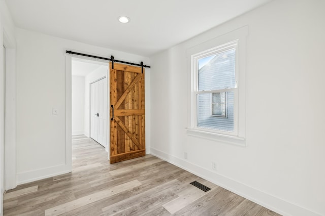 spare room with a barn door and light hardwood / wood-style floors