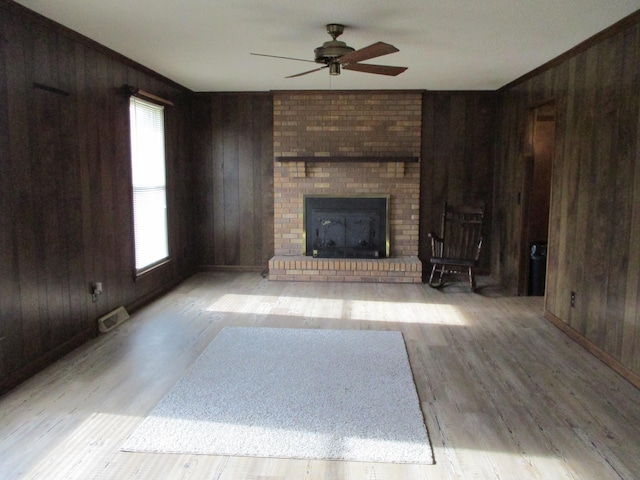 unfurnished living room with a fireplace, wood walls, light hardwood / wood-style flooring, and ceiling fan