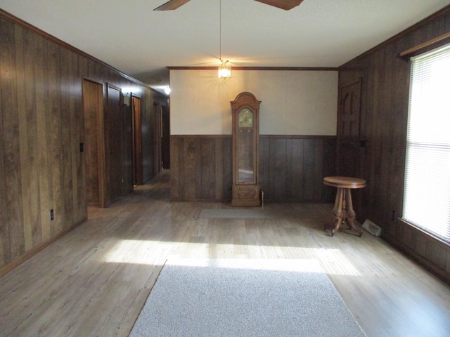 spare room featuring ceiling fan, crown molding, wooden walls, and light hardwood / wood-style flooring