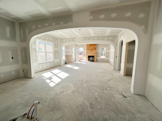 unfurnished living room featuring arched walkways, a fireplace, and plenty of natural light