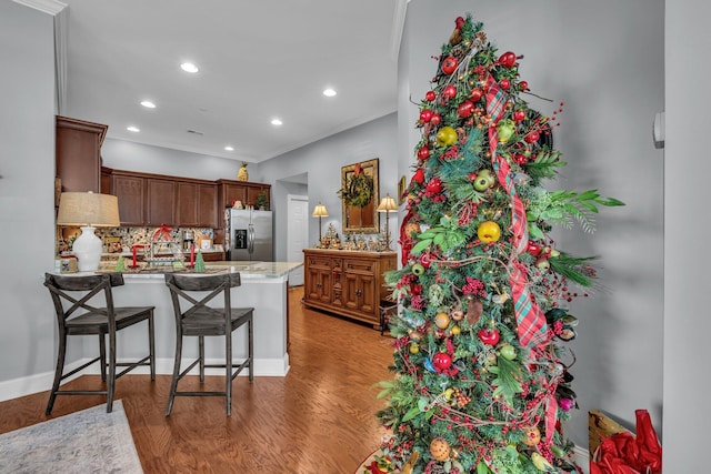 kitchen with kitchen peninsula, hardwood / wood-style flooring, decorative backsplash, ornamental molding, and stainless steel fridge with ice dispenser