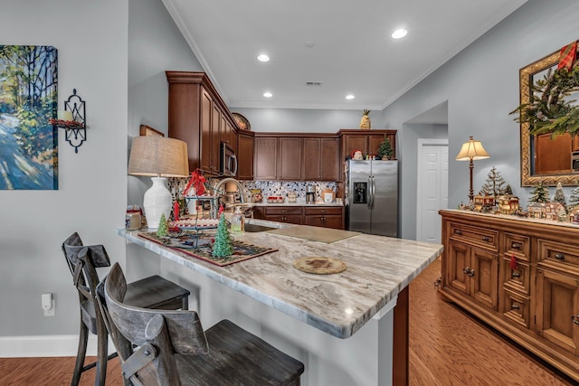 kitchen featuring a breakfast bar, light hardwood / wood-style flooring, ornamental molding, tasteful backsplash, and stainless steel appliances