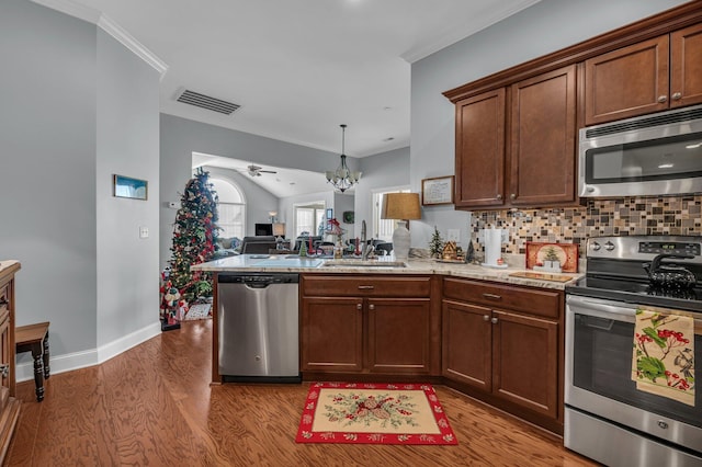 kitchen featuring backsplash, light wood-type flooring, ornamental molding, kitchen peninsula, and stainless steel appliances