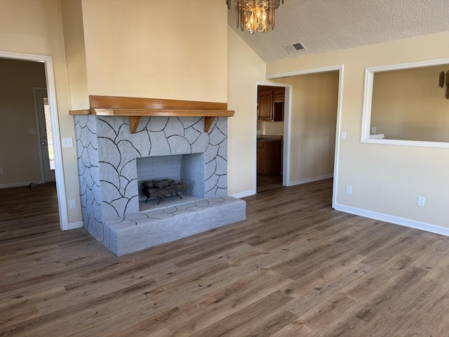 unfurnished living room featuring hardwood / wood-style floors, a stone fireplace, lofted ceiling, and a textured ceiling