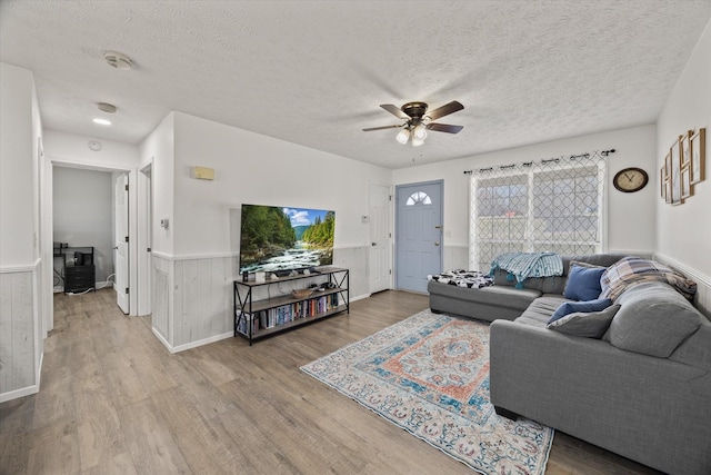 living room with ceiling fan, wood walls, wood-type flooring, and a textured ceiling