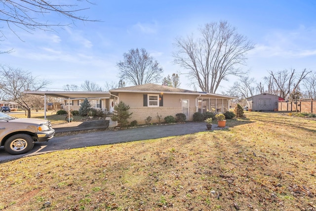 single story home featuring a front yard, a storage unit, a carport, and a sunroom