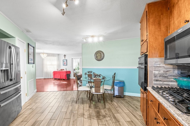 kitchen featuring rail lighting, stainless steel appliances, tasteful backsplash, a chandelier, and light wood-type flooring