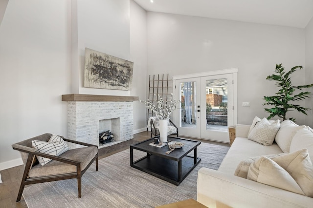 living room with hardwood / wood-style flooring, a brick fireplace, a high ceiling, and french doors