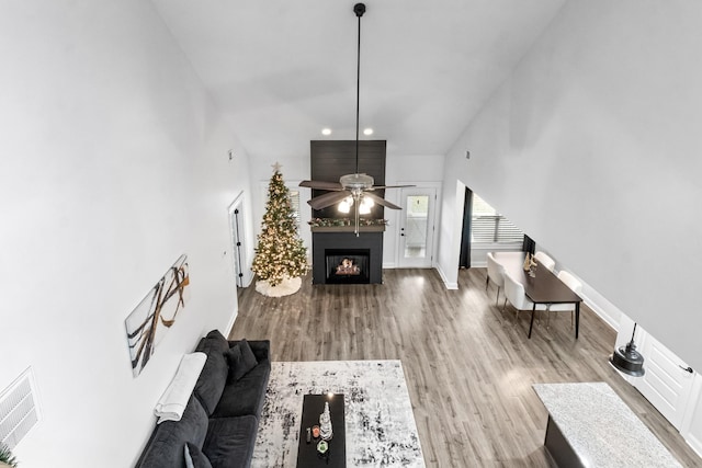 living room with a towering ceiling, a lit fireplace, visible vents, and wood finished floors