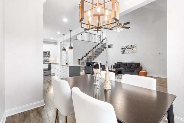 dining space featuring recessed lighting, stairway, wood finished floors, baseboards, and ceiling fan with notable chandelier