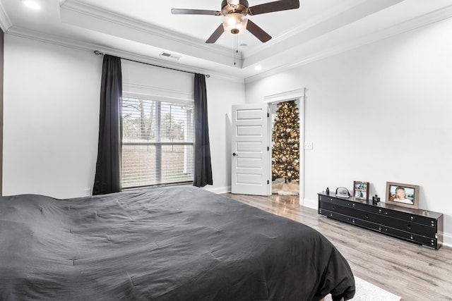 bedroom with visible vents, a tray ceiling, crown molding, and wood finished floors