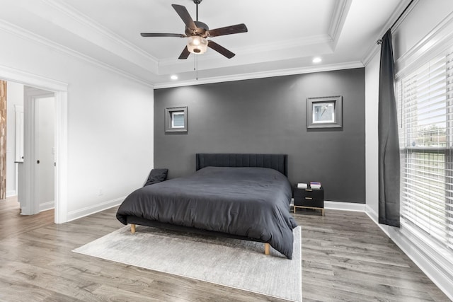 bedroom featuring baseboards, ornamental molding, a raised ceiling, and wood finished floors