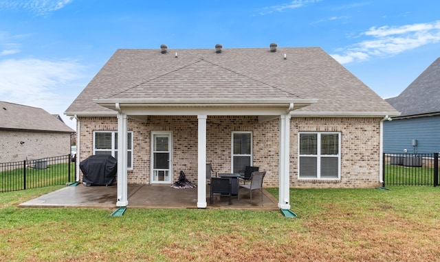 back of property featuring roof with shingles, a yard, brick siding, and a patio