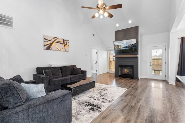 living room featuring high vaulted ceiling, a fireplace, wood finished floors, visible vents, and baseboards