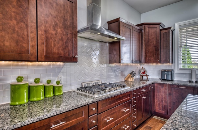 kitchen featuring decorative backsplash, wall chimney exhaust hood, stone counters, hardwood / wood-style floors, and stainless steel gas stovetop