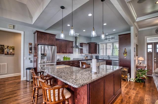 kitchen with light stone countertops, wall chimney exhaust hood, hanging light fixtures, stainless steel appliances, and a kitchen island