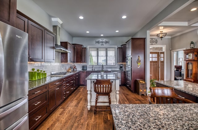 kitchen featuring a center island, wall chimney exhaust hood, dark stone countertops, appliances with stainless steel finishes, and dark hardwood / wood-style flooring