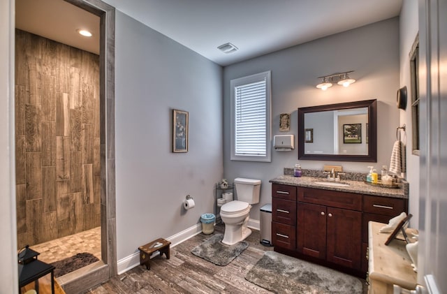 bathroom featuring vanity, toilet, wood-type flooring, and tiled shower