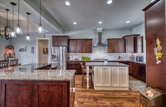 kitchen with a center island, light stone counters, wall chimney range hood, and appliances with stainless steel finishes