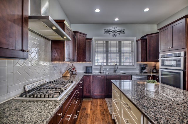 kitchen with dark wood-type flooring, dark stone counters, sink, wall chimney exhaust hood, and appliances with stainless steel finishes