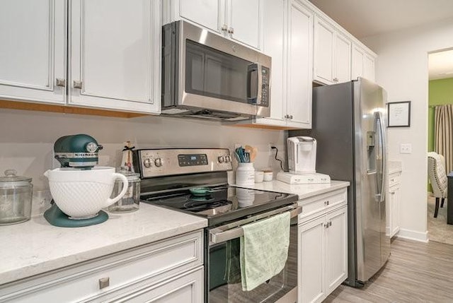 kitchen with light stone counters, white cabinetry, stainless steel appliances, and light hardwood / wood-style flooring