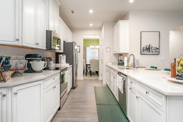 kitchen with an inviting chandelier, sink, light wood-type flooring, appliances with stainless steel finishes, and white cabinetry