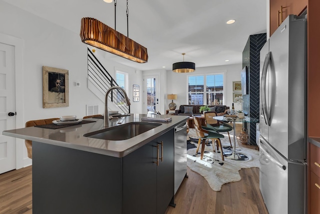 kitchen featuring sink, wood-type flooring, decorative light fixtures, a kitchen island with sink, and appliances with stainless steel finishes