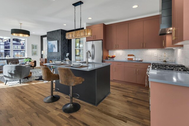 kitchen featuring dark hardwood / wood-style flooring, stainless steel fridge, a center island with sink, and decorative light fixtures